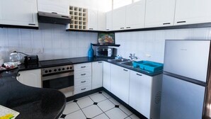 A modern kitchen with white cabinets, a black countertop, a stove, a sink, and a refrigerator. - Coastal Retreat | Terrace | Pool | Sea Views (Margate)