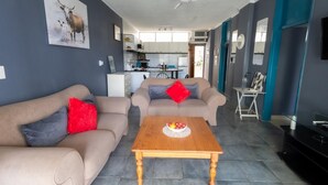 A modern living room with two sofas, a wooden coffee table with fruit, a TV, and a kitchen in the background. - Coastal Retreat | Terrace | Pool | Sea Views (Margate)