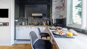 Una cocina moderna con una paleta de colores blanco y negro, una pared de acento de piedra y una zona de comedor con alimentos para el desayuno.