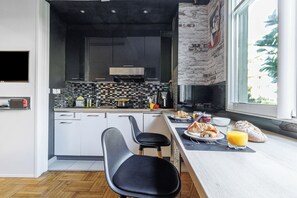 Eine moderne Küche mit Schwarz-Weiß-Farbgebung, einer Wand mit Steinakzenten und einem Essbereich mit Frühstücksangeboten.