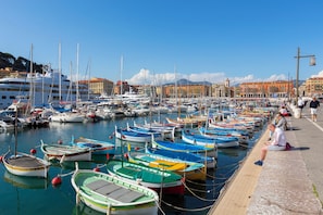Un port de plaisance où sont amarrés de nombreux bateaux, une promenade en bord de mer et des bâtiments en arrière-plan.