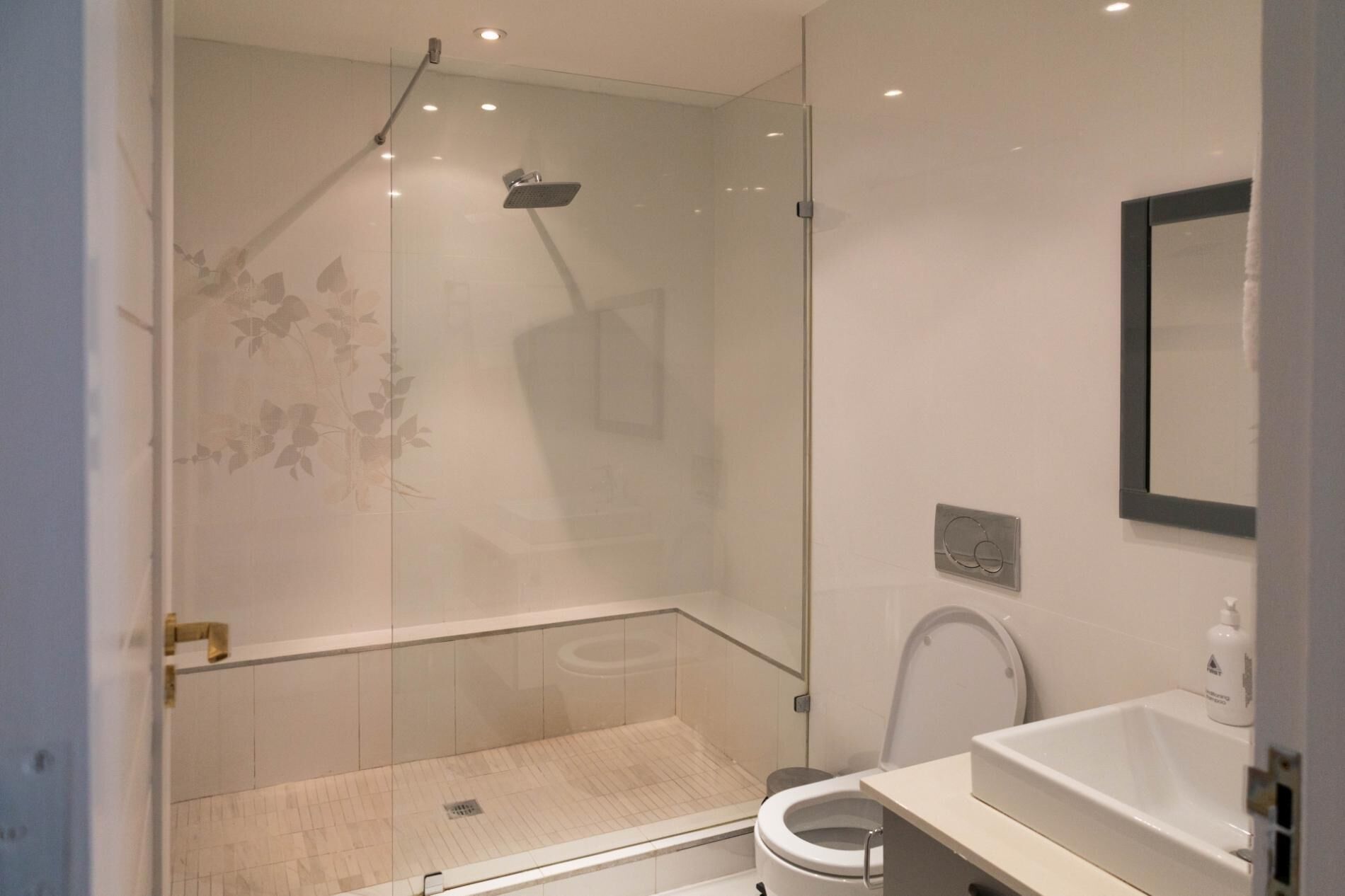A modern bathroom with a glass-enclosed shower, a toilet, and a sink.
