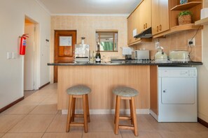 A modern kitchen with wooden cabinets, a built-in dishwasher, and two bar stools. - Luxury Riverside Views | Balcony | Pool (Velddrif)