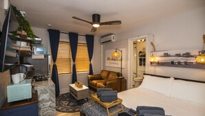 Une chambre d’hôtel moderne équipée d’un lit, d’un canapé, d’une petite table, d’une télévision, d’un ventilateur de plafond et d’une fenêtre avec des stores.