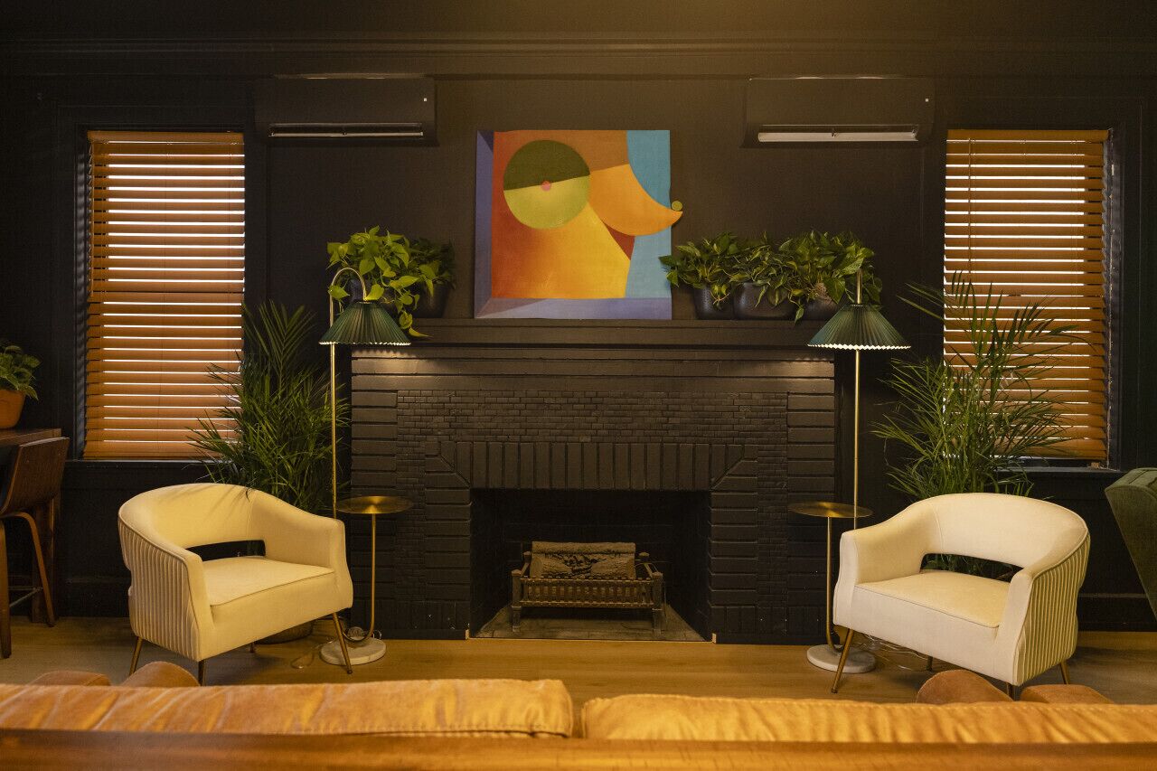 A living room with a fireplace, two armchairs, a sofa, and a painting on the wall.