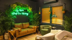 Een knus interieur met een neonbord, een bank, fauteuils en potplanten.
