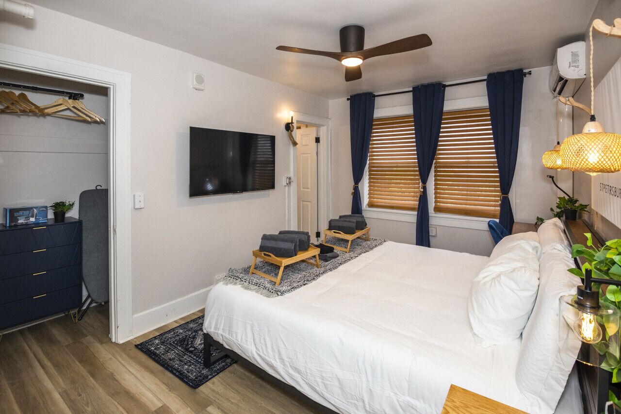 Een slaapkamer met een bed, twee fauteuils, een plafondventilator, een televisie en een raam met gordijnen.