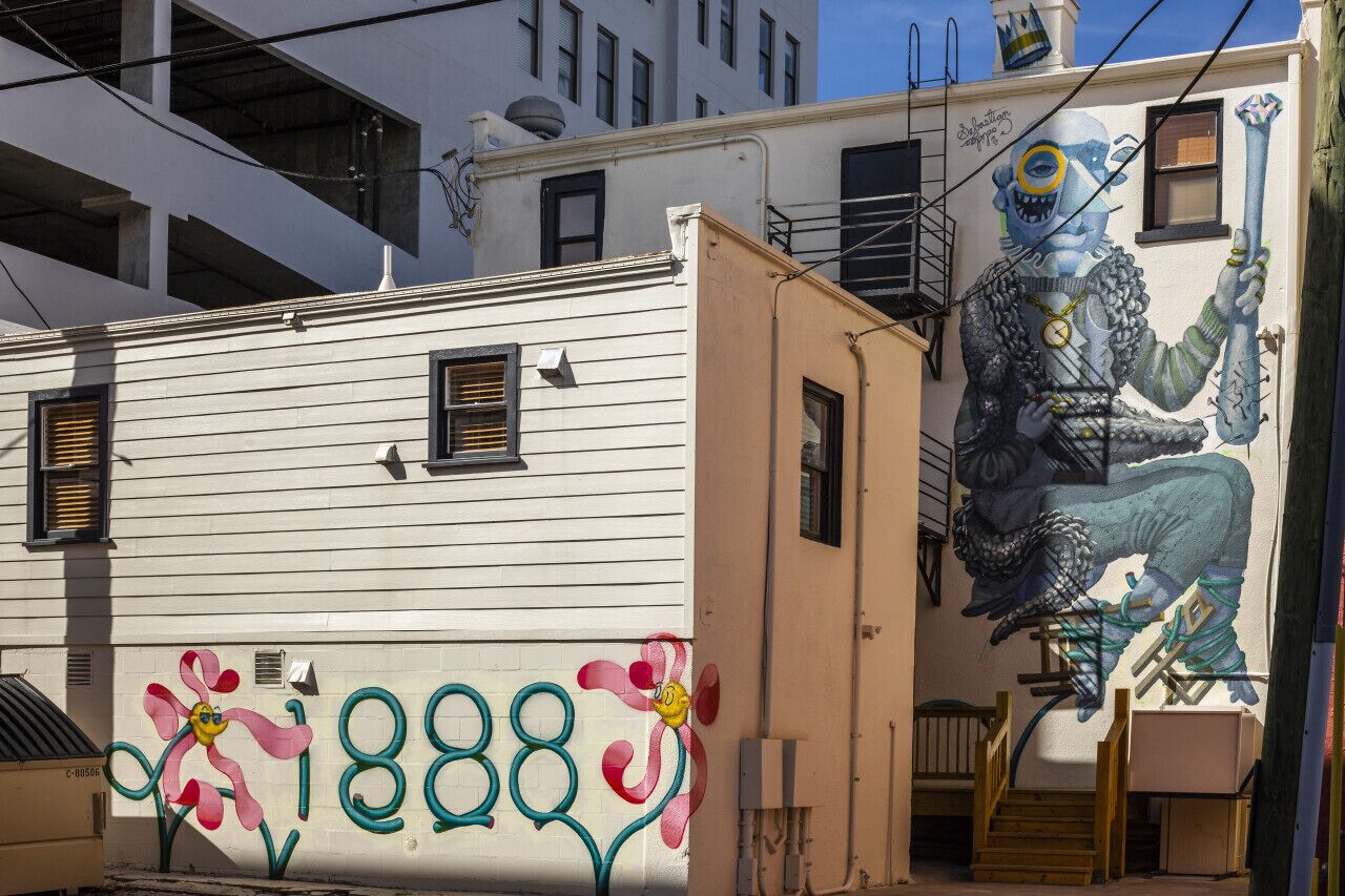 Un edificio con un mural que muestra una figura sosteniendo un báculo y un reloj, y el número 1888 pintado en la pared.