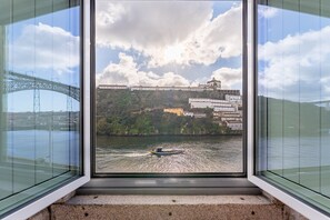 Blick aus einem Fenster auf einen Fluss mit einer Brücke und Gebäuden am gegenüberliegenden Ufer.