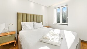 A modern bedroom with a large bed, a nightstand, a lamp, and a window with a view of trees. - GuestReady - Urban comfort with Douro River view (Porto)