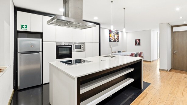 A modern kitchen with a stainless steel refrigerator, oven, and microwave, a large island with a sink, and pendant lighting. - GuestReady - Urban comfort with Douro River view (Porto)