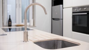 A modern kitchen with a stainless steel faucet, a built-in sink, and a refrigerator in the background. - GuestReady - Urban comfort with Douro River view (Porto)