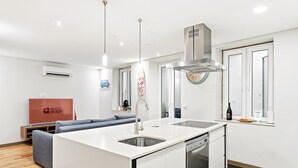 A modern kitchen with a central island, a built-in dishwasher, and a stainless steel range hood. - GuestReady - Urban comfort with Douro River view (Porto)