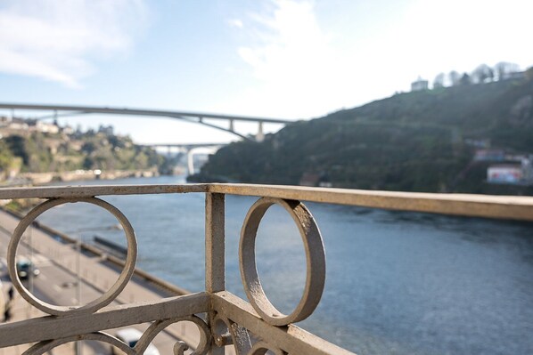 Barandilla de metal con diseños circulares, con vistas a un río, un puente y colinas al fondo.