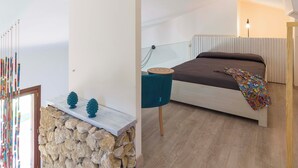 Ein Schlafzimmer mit einem Bett, einer Steinwand, einem blauen Sessel und einem Zier-Spiegel.