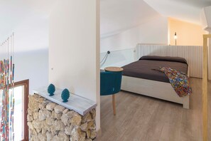 A bedroom with a bed, a stone wall, a blue chair, and a decorative mirror. - Villa Guidaloca, sea view and pool (Castellammare del Golfo)