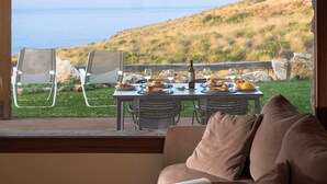 A dining table set with plates, glasses, and a bottle, overlooking a grassy hillside and the sea. - Villa Scogliera with sea view and pool (Castellammare del Golfo)