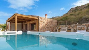 A modern outdoor pool area with a stone wall and wooden pergola. - Villa Scogliera with sea view and pool (Castellammare del Golfo)