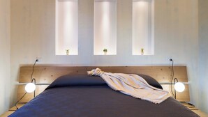 A bedroom with a bed, bedside lamps, and three windows with plants. - Villa Scogliera with sea view and pool (Castellammare del Golfo)