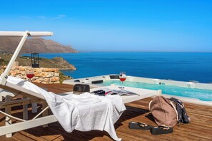 Un terrazzo in legno con una poltrona da relax, un tavolino con un bicchiere di vino, un libro e una borsa.