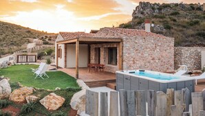A stone house with a patio, a hot tub, and a view of a rocky hillside. - Villa Zingaro with sea view and pool (Castellammare del Golfo)