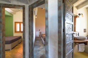 A bedroom with a bed, a bathroom with a sink and mirror, and a hallway with a door. - Villa Scopello with sea view and pool (Castellammare del Golfo)
