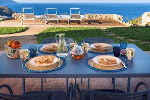 A table set for breakfast with plates of food, a pitcher, and cups, overlooking a scenic ocean view. - Villa Scopello with sea view and pool (Castellammare del Golfo)