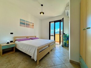Quarto com cama, mesa de cabeceira e vista para o exterior.