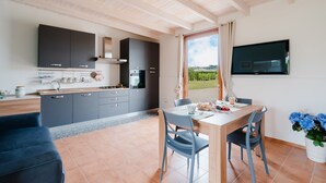 Een moderne keuken met grijze kastjes, een eethoek met een gedekte tafel voor twee personen, en een groot raam met uitzicht op een wijngaard.