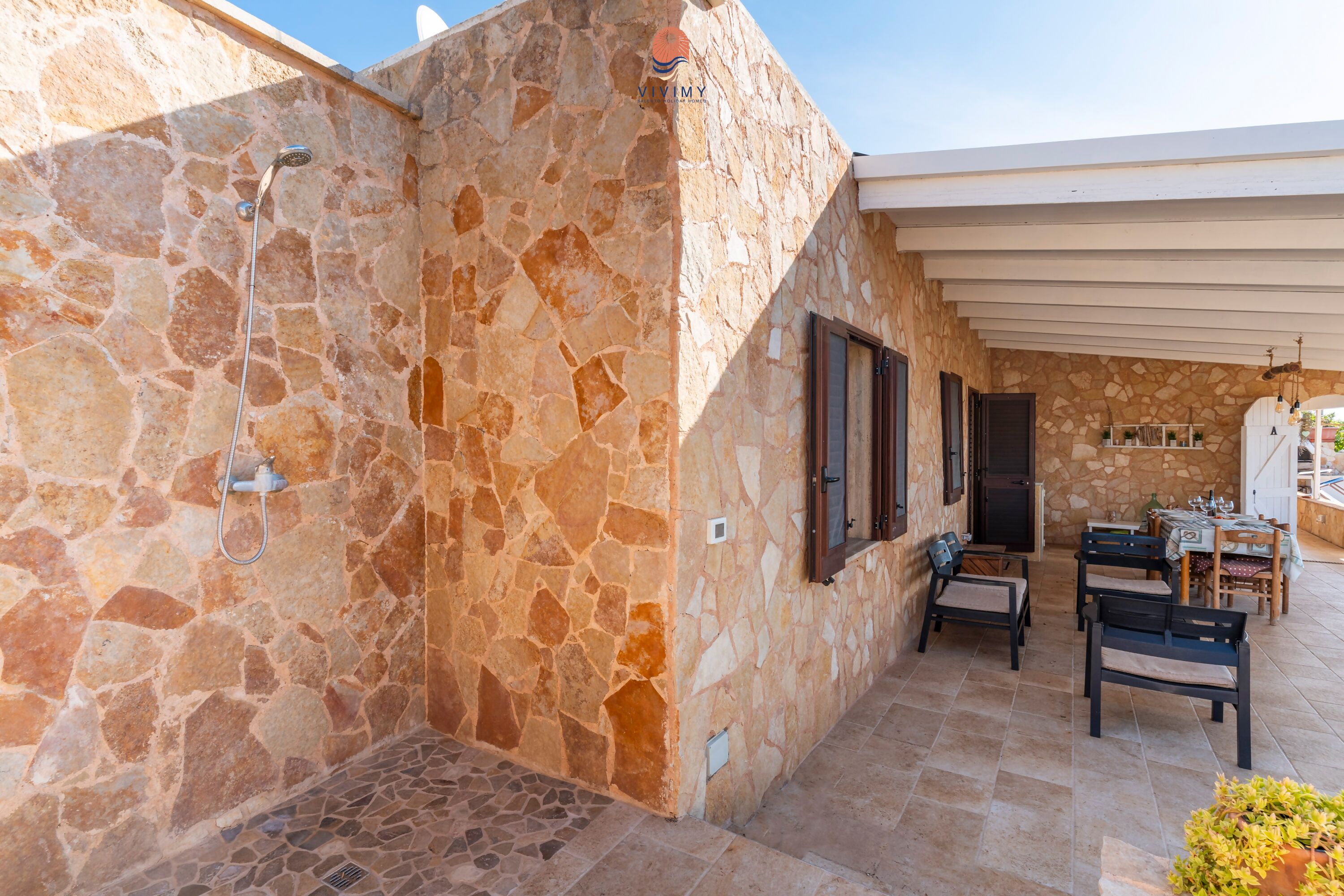A stone-walled outdoor area with a shower, seating, and a covered patio.
