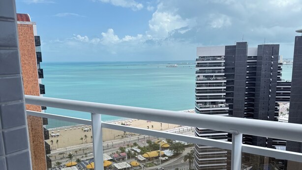 Un balcon avec vue sur la plage, les bâtiments et un ciel dégagé.