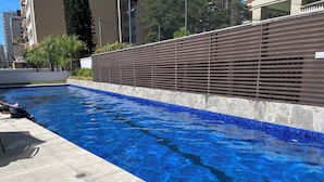 Une piscine à l’eau d’un bleu cristallin, une terrasse carrelée et une clôture moderne.
