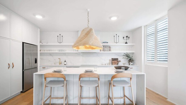 Een moderne keuken met witte kastjes, een centraal eiland met barkrukken en een hangende lamp.