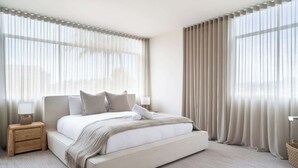 Een moderne slaapkamer met een groot bed, een nachtkastje en lichte gordijnen.