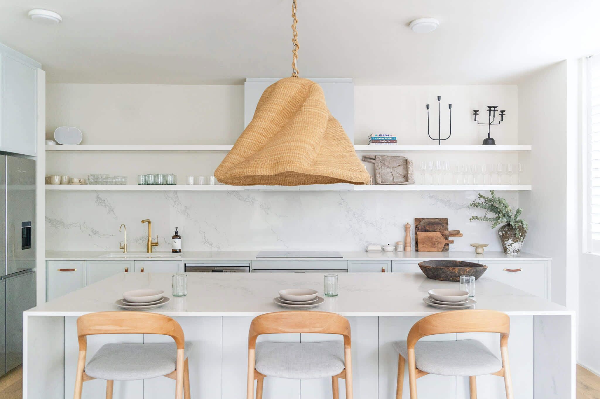 Una cocina moderna con una isla central, muebles blancos y una lámpara colgante.