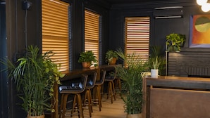 Een bar met houten stoelen en tafels, omringd door plantenpotten.