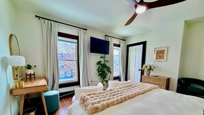 Une chambre à coucher avec un lit, un bureau, une chaise, un téléviseur et une fenêtre avec des rideaux.