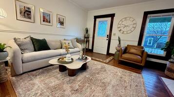 A living room with a sofa, a coffee table, a brown leather chair, a clock, and framed pictures on the wall.