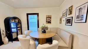 Un coin repas comprenant une table ronde, quatre chaises, un banc, une bibliothèque et des tableaux encadrés accrochés au mur.