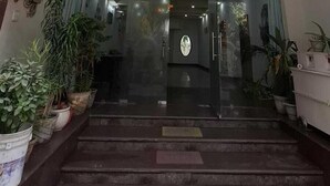 A building entrance with a glass door, steps leading up to it, and potted plants on either side. - Taj homes - A Unit of Sahni's Villa (Gurugram)