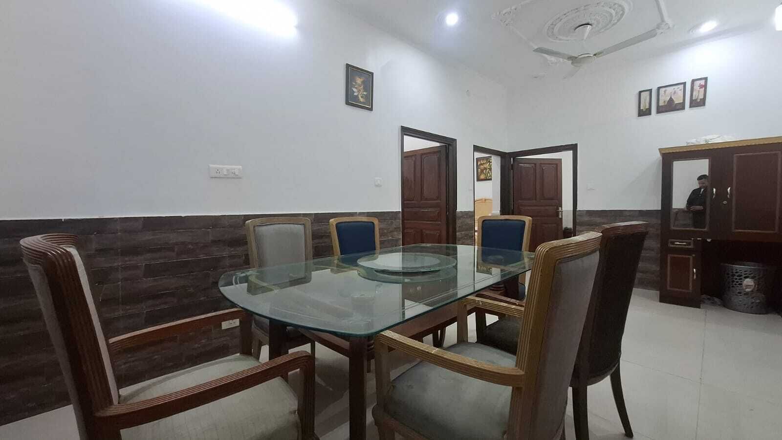 Un comedor con una mesa de vidrio rodeada por sillas de madera, una pared de madera oscura y una puerta que da a otra habitación.