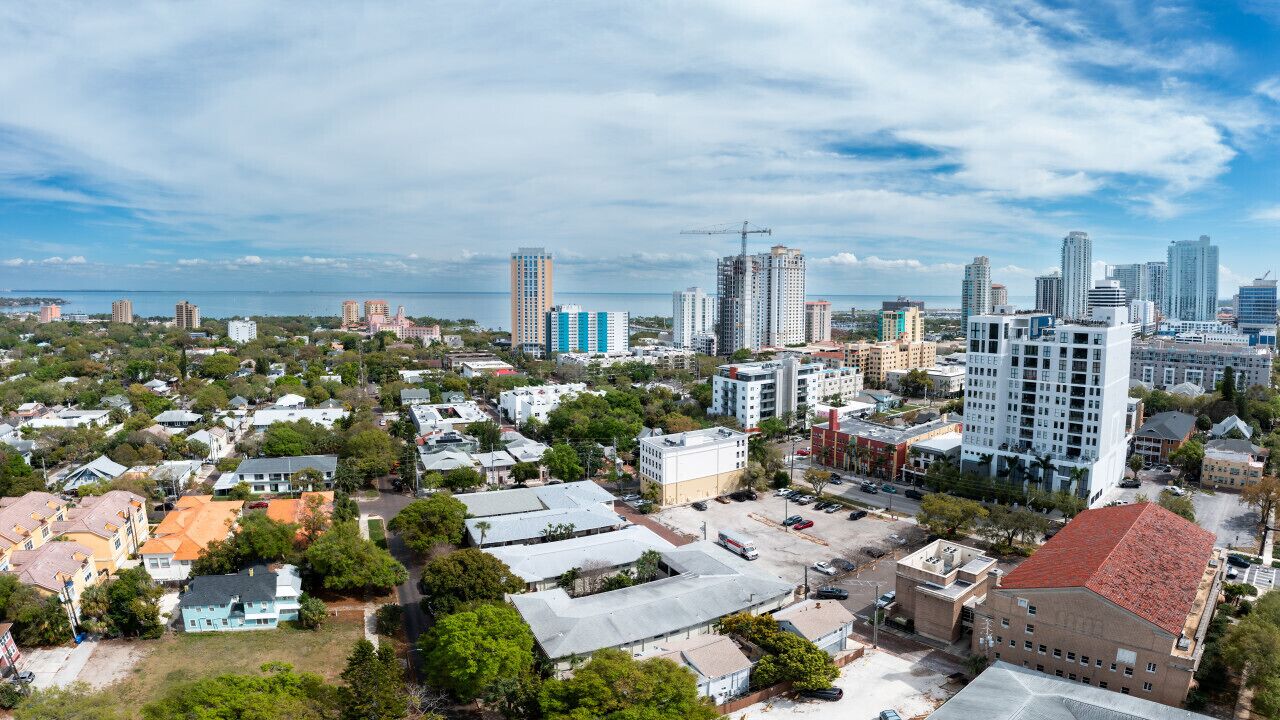 A cityscape with high-rise buildings, a mix of residential and commercial structures, and a body of water in the distance.