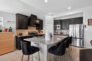 Una cocina moderna con armarios oscuros, una isla central con taburetes altos, un refrigerador de acero inoxidable y un cartel de café en la pared.