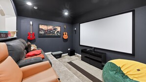 Une salle de cinéma maison équipée d’un grand écran, de deux guitares, d’un fauteuil-sac et d’un canapé.