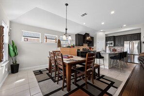 Una cocina moderna con armarios oscuros, un refrigerador de acero inoxidable y un comedor con una mesa y sillas de madera.