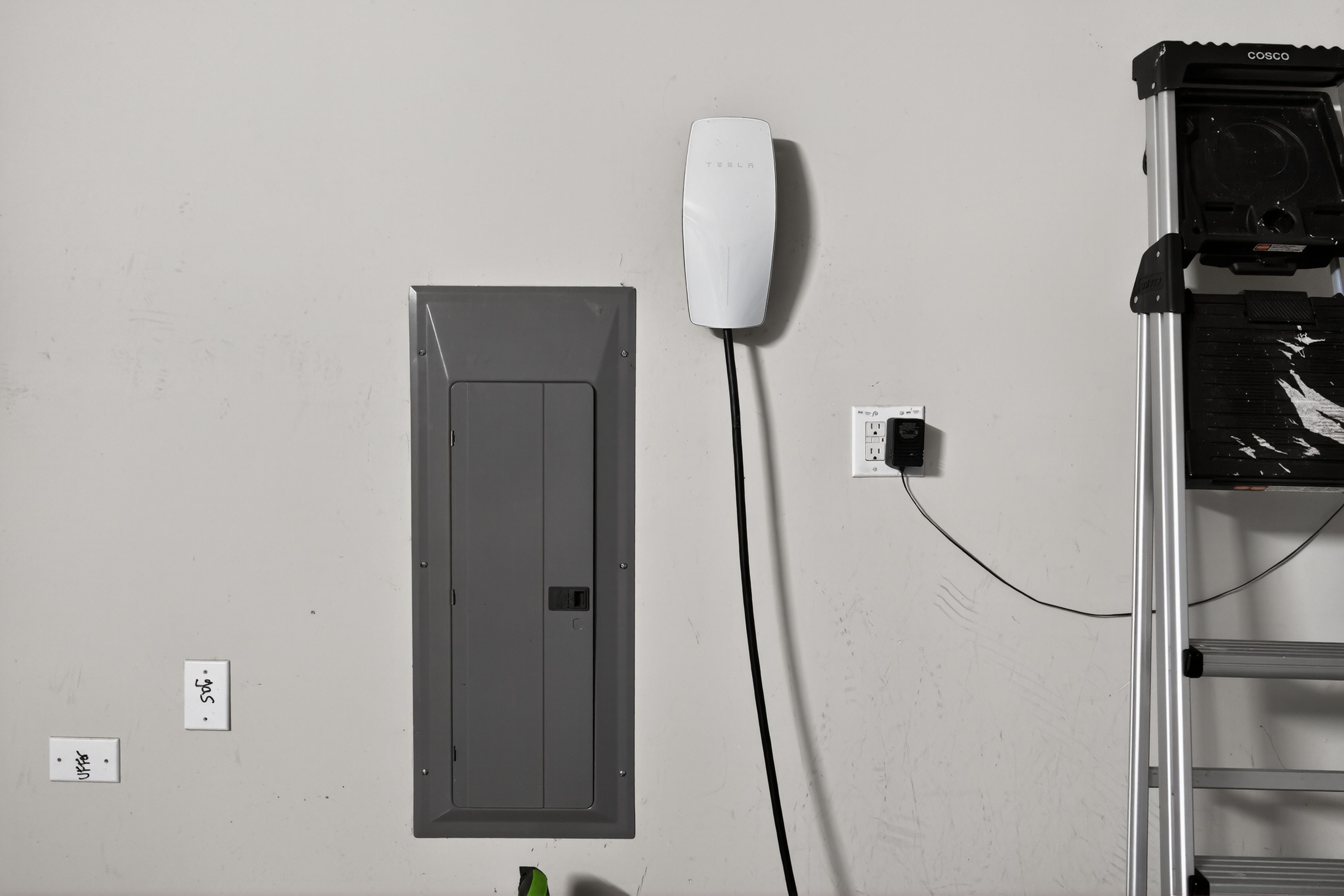 A wall-mounted electrical box, a white plug, and a metal ladder.