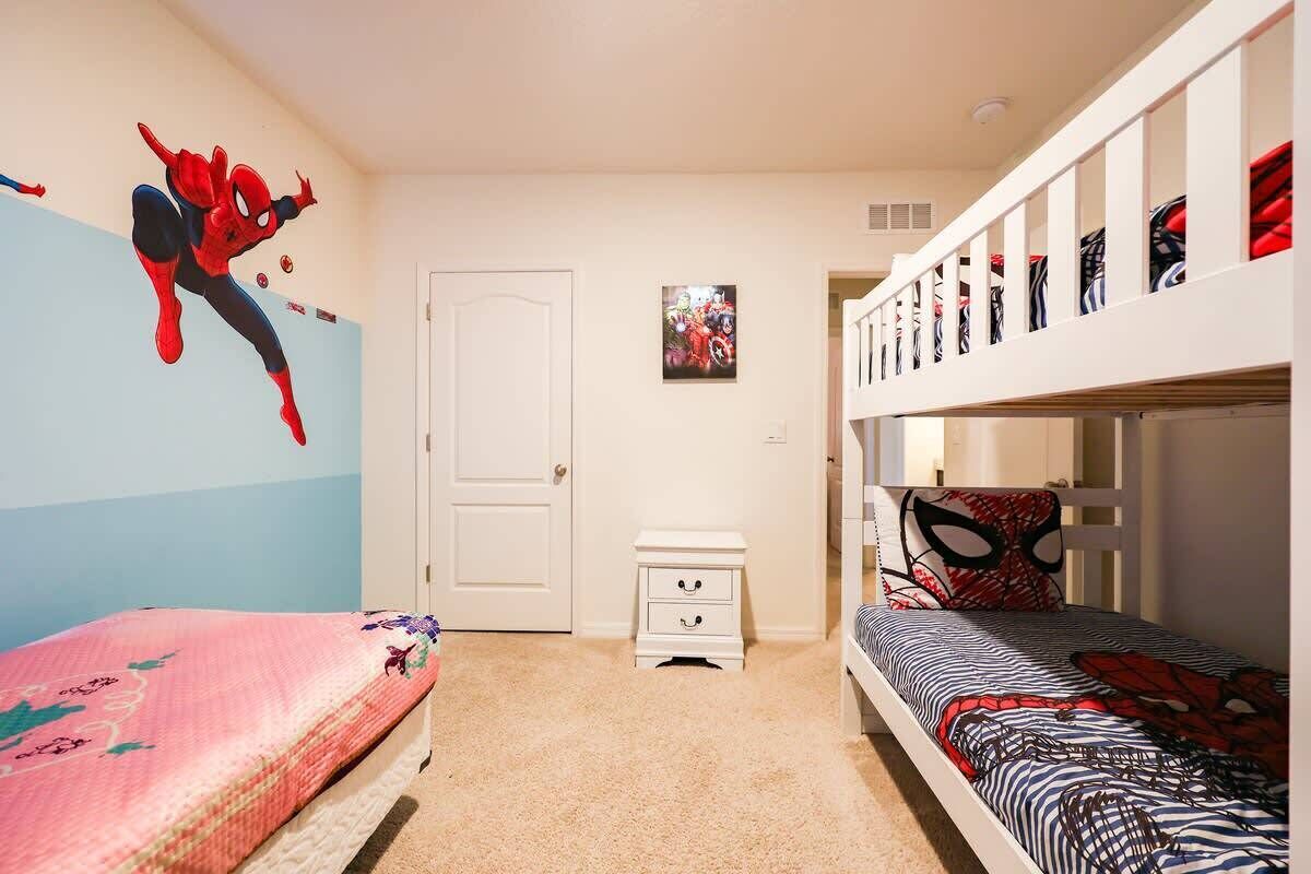 A child's bedroom with bunk beds, a door, a small bedside table, and a wall mural.