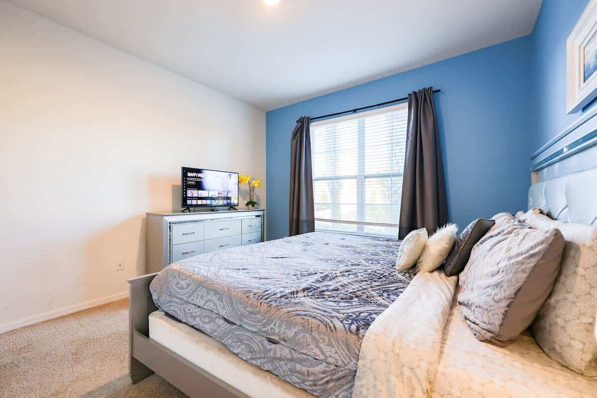 Une chambre à coucher avec un lit, une télévision, une commode et une fenêtre avec des rideaux.