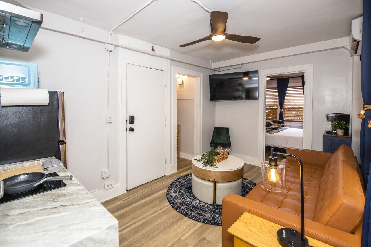 A compact living space with a kitchenette, a round coffee table, a sofa, and a ceiling fan.