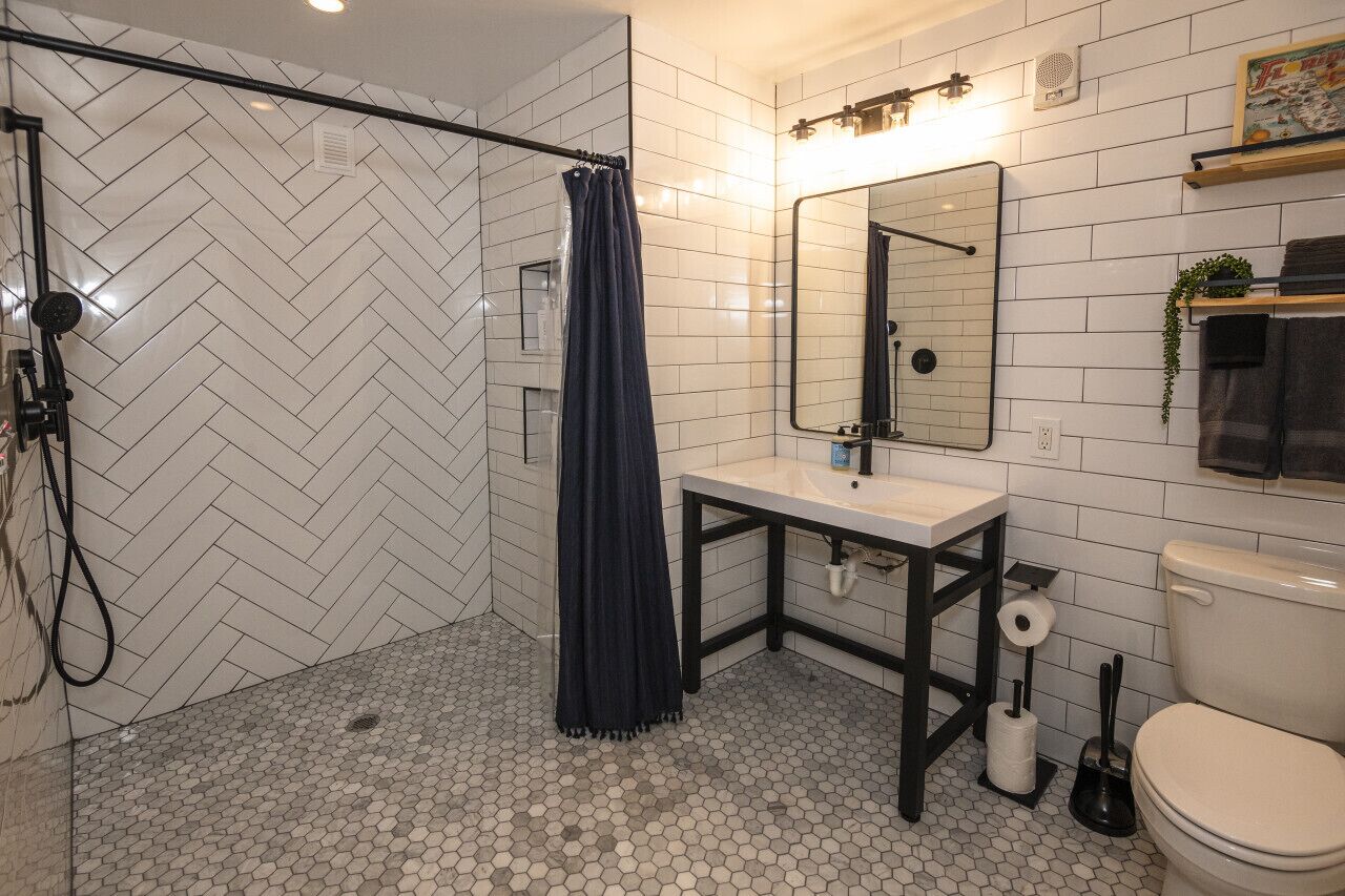 Een moderne badkamer met een backsplash van visgraat tegels, een douche met gordijn, een wastafel met spiegel, en een toilet.